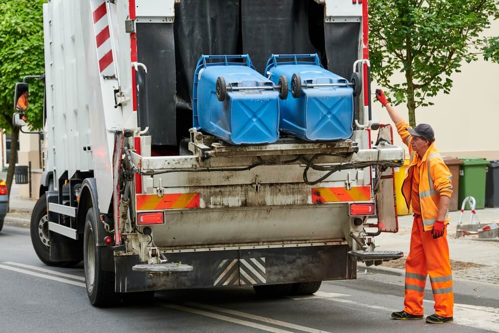 shutterstock_2175765903 (1) Two blue bins getting emptied into garbage truck